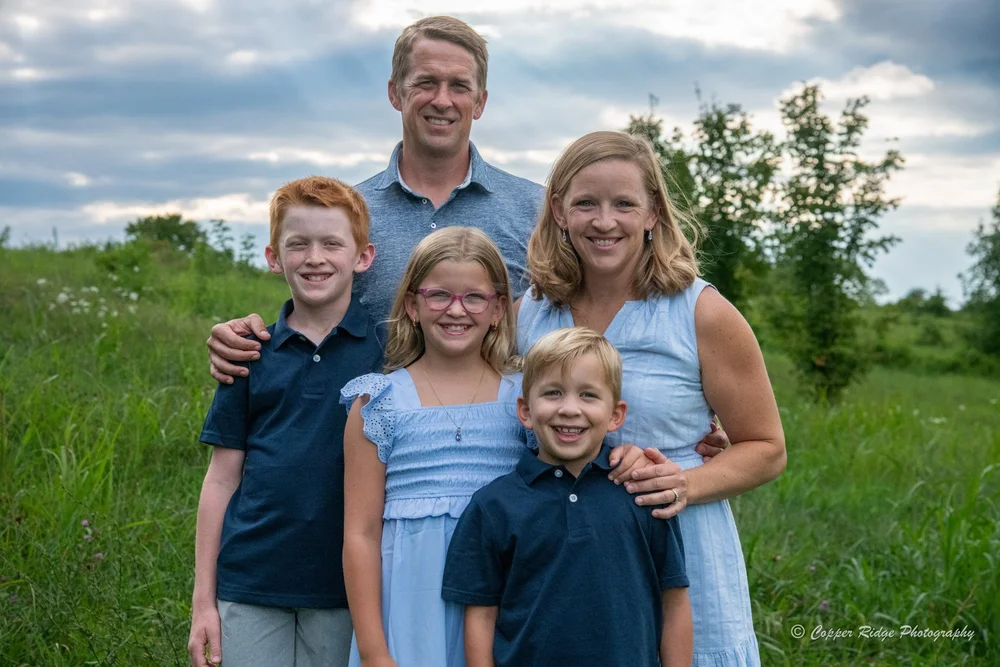 A family of five in a wildflower field under a dramatic evening sky