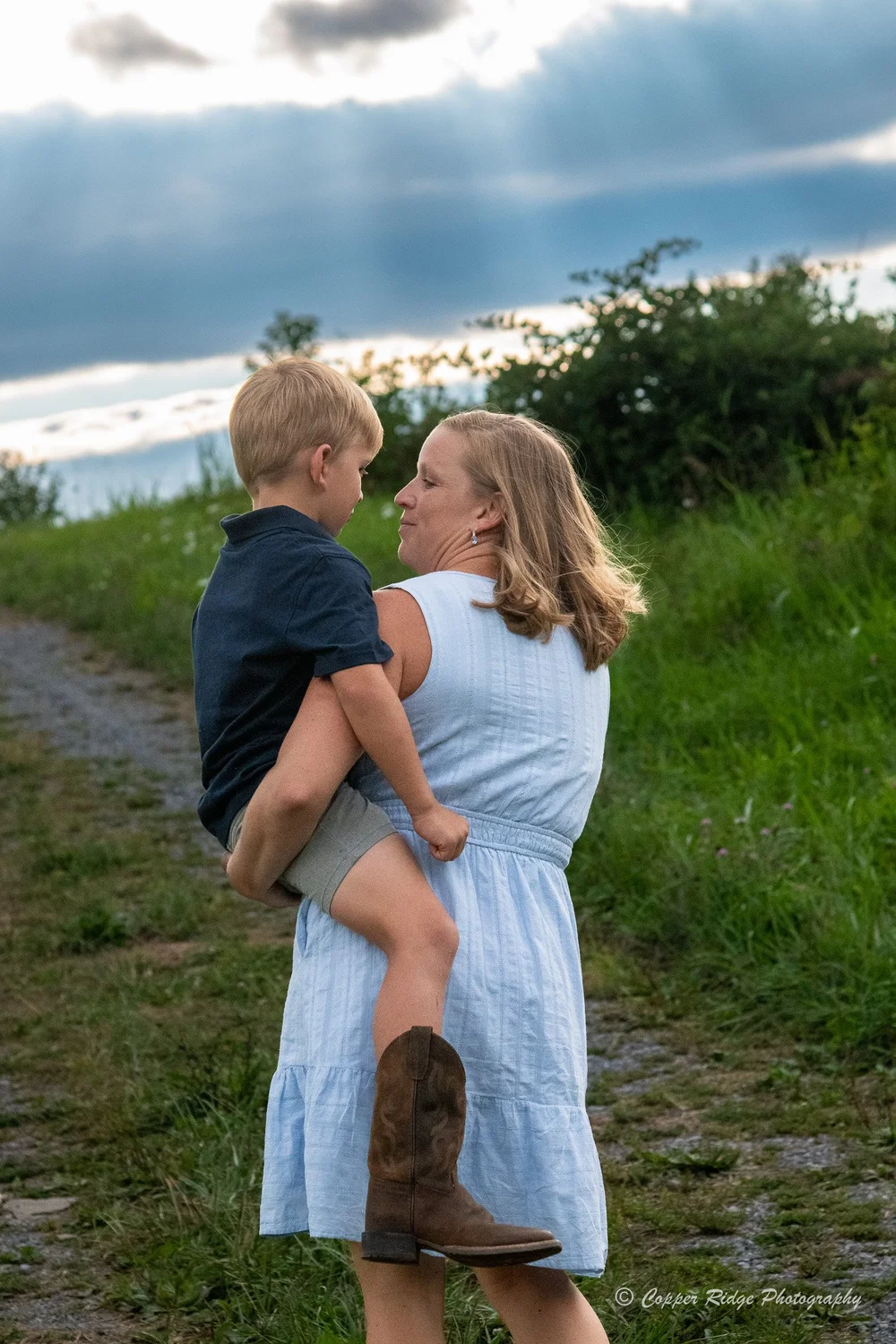 A mother holding her young son on a country lane at golden hour