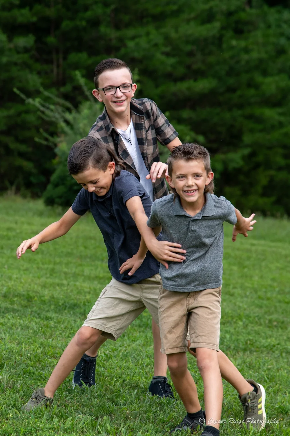 Three brothers laughing and playing together in a green field