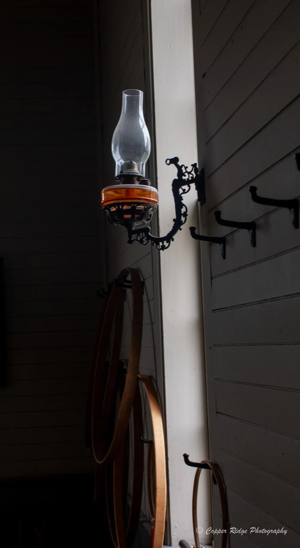 An antique oil lamp on a whitewashed wall in soft window light